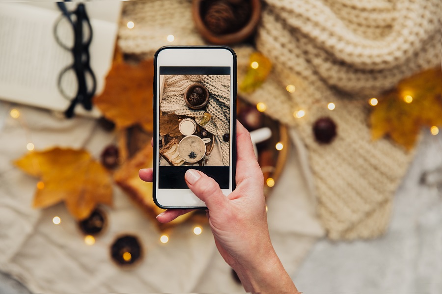 Instagram photography blogging concept. hand holding phone taking photo of stylish winter flat lay. cozy mood autumn.